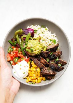 a person is holding a plate with meat, rice and veggies on it