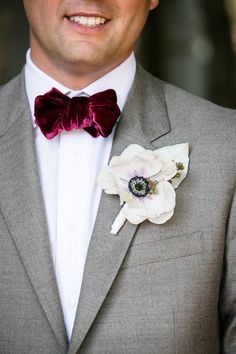 a man wearing a gray suit with a red bow tie and flower in his lapel