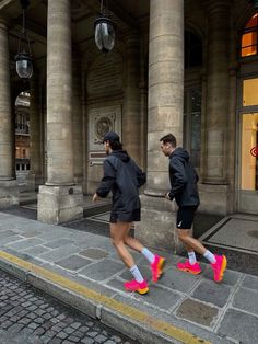 two people walking down the street in front of a building with columns and pillars on either side