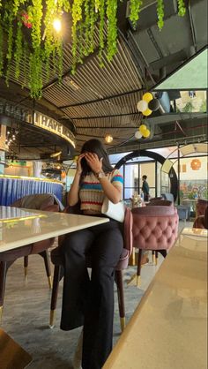 a woman sitting at a table with her hand on her face while talking on the phone