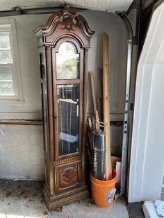 an old grandfather clock sitting in the corner of a room next to a trash can