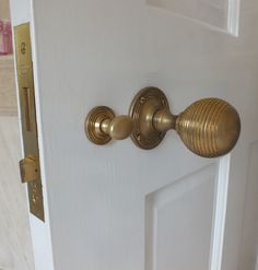 an open door with brass knobs in a home bathroom area that is white and has beige tile flooring