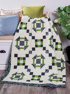 a green and white quilt sitting on top of a wooden floor next to a potted plant