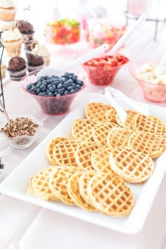 some waffles and blueberries are on a white plate next to cupcakes