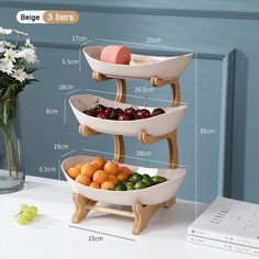 three tiered serving tray with fruit and vegetables in it on a table next to a vase