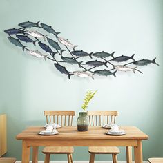 a dining room table with two chairs and a metal fish wall decoration on the wall