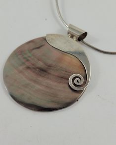 A vintage  round shell disc with hand-made sterling silver half bezel on a 16 inch sterling tube chain.  SKU-1595 This is a lovely vintage necklace with a iridescent round shell.  The disc is mother of pearl with brown, and pink tones resembling bronze.  The disc has a sterling silver stylized half bezel, and a large tube  bail.  A 1.5 mm wide tube chain which measure 16 inches holds the gorgeous disc. D E T A I L S : Measures  :  Tube chain is approx. 16 in / 40.6 cm  long x  1.5 mm diameter Sh Silver Mother Of Pearl Round Shell Necklace, Silver Round Mother Of Pearl Shell Necklace, Silver Round Shell Necklace For Gifts, Silver Mother Of Pearl Shell Necklace, Vintage Round Mother Of Pearl Necklace, Vintage Sterling Silver Necklace, Half Bezel, Brown And Pink, Wedding Jewellery Necklace