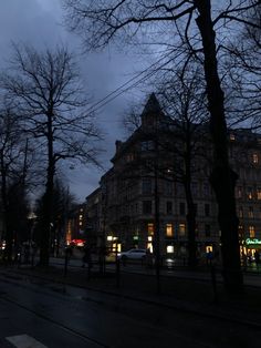 an empty city street at night with tall buildings and trees in the foreground, on a cloudy day