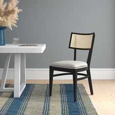 a chair sitting on top of a blue rug next to a white table and vase