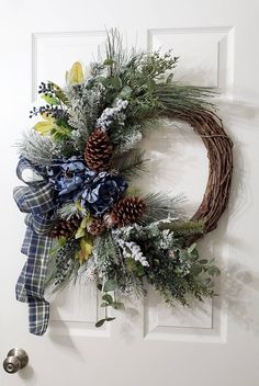 a wreath with pine cones and blue flowers hangs on the front door's white door