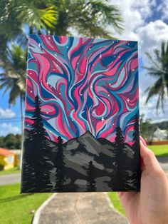 a hand holding up a piece of art that looks like mountains and trees with colorful swirls