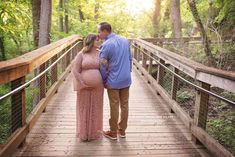 a pregnant couple standing on a bridge in the woods