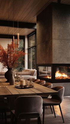 a dining room table with chairs and a fire place in the fireplace behind it, surrounded by large windows