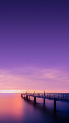 a long pier sitting on top of a large body of water under a purple sky