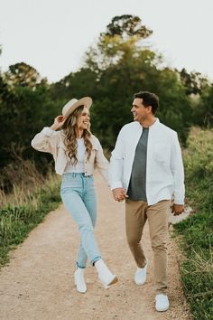 a man and woman walking down a dirt road holding hands