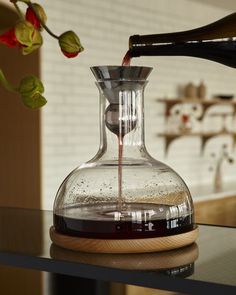 a glass vase filled with liquid on top of a wooden table next to a potted plant