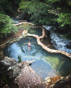 a person swimming in a river surrounded by rocks and trees with water running through it