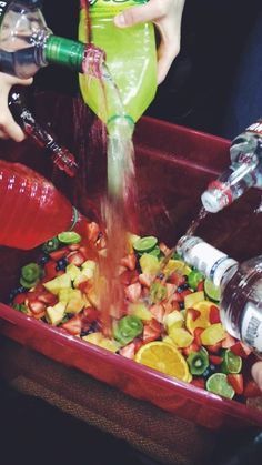 two people are filling bottles into a red container filled with fruit and veggies