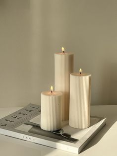 three white candles sitting on top of a table next to a ruler and pencils