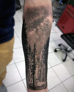 a man's arm with a forest scene on it and stars in the sky