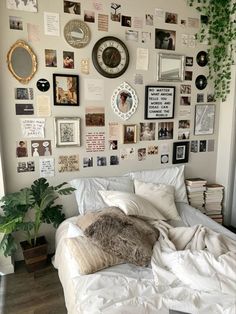 a bed with white sheets and lots of pictures on the wall above it, along with a potted plant