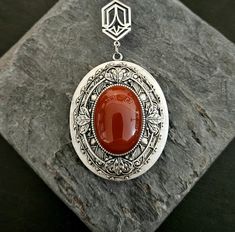 A dreamy red carnelian oval centered on layers of intricate antiqued silver filigree and a frame set on a large antiqued silver locket. Locket hangs from an antiqued silver art deco connector and a long antiqued silver chain with a 2 inch extender. Extender has a small genuine red carnelian bead on the end as shown. Locket opens with 2 spaces for pictures as shown.  Details: Locket measures 2 x 1.5 inches Inner area of locket measures approx 31mm x 24mm Locket has a smooth back as shown Pendant hangs 3 inches Locket and chain are plated brass Necklace measures 28 inches (+2 inch extender) Stone is genuine red carnelian Please allow for possible slight color differences due to different settings on different screens. Want a shorter chain? Just leave a note to seller at checkout for me and I Red Cameo Oval Jewelry, Elegant Carnelian Jewelry With Large Pendant, Elegant Carnelian Oval Pendant Jewelry, Cameo Carnelian Jewelry Gift, Carnelian Cameo Jewelry Gift, Antique Oval Carnelian Jewelry, Handmade Antique Silver Elegant Locket Necklace, Necklace Gift Ideas, Art Deco Locket