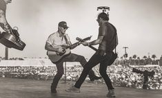 two men are playing guitars on stage in front of an audience at a music festival