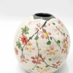 a white vase with colorful flowers painted on the outside and inside, sitting on a white surface