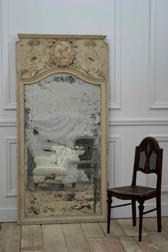 an old chair sitting in front of a large mirror on the floor next to a wooden chair