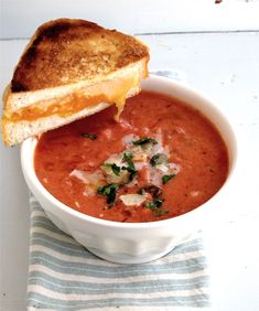 a white bowl filled with soup next to a piece of bread on top of a blue and white towel