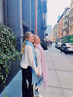 two women standing next to each other in front of a building on a city street