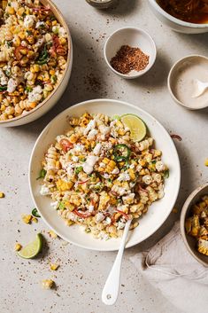 a white plate topped with corn next to two bowls filled with soup and seasonings