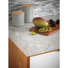 a cutting board topped with sliced fruit on top of a counter next to stacks of plates