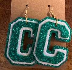 green and white earrings with the letter c on it's earwires sitting on top of a piece of cardboard