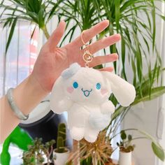 a person holding up a stuffed animal keychain in front of a potted plant