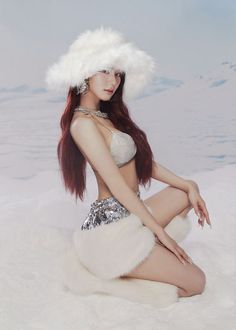 a woman with long red hair sitting in the snow wearing a white fur hat and silver sequins