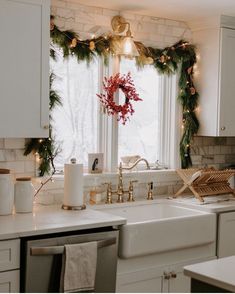 a kitchen decorated for christmas with wreaths and lights on the window sill above the sink