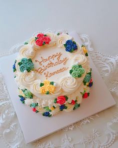 a birthday cake with white frosting and multicolored roses on it sitting on top of a doily