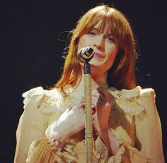 a woman with red hair holding a microphone in front of her face and wearing a white dress