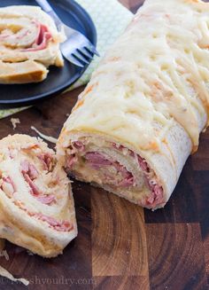 a ham and cheese roll cut in half on a cutting board next to a fork