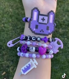 a person wearing purple bracelets with charms on their wrist and the word stick in front of them