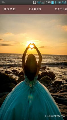 a woman in a blue dress making a heart shape with her hands on the beach