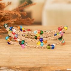 two bracelets with multicolored beads sitting on top of a wooden table next to a potted plant