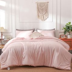 a bed with pink comforter and pillows in a white room next to a table