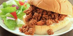 a sloppy joe sandwich on a plate with lettuce and tomato salad in the background