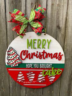 a merry christmas sign hanging on the side of a wooden fence next to a green and red bow