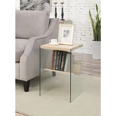 a glass side table with books on it in front of a couch and potted plant