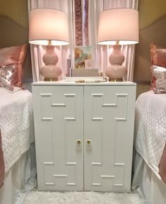 two white nightstands sitting next to each other with pink lamps on top of them