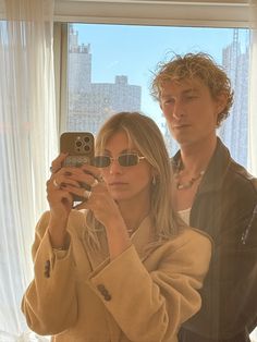 a man and woman standing in front of a window taking a photo with their cell phone