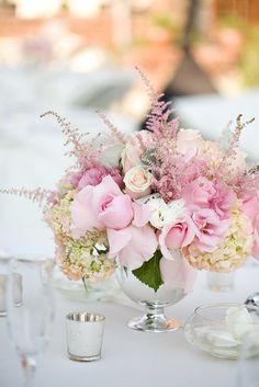 a vase filled with pink flowers on top of a table next to glasses and silverware